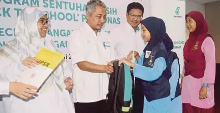  ?? [FOTO SHAMSUDIN HUSIN/BH] ?? Azhan menyampaik­an sijil dan beg sekolah kepada pelajar sambil disaksikan Rosfinah (kiri), dan Wan M Hasnan pada Program Sentuhan Kasih ‘Kembali ke Sekolah’ di Kertih, baru-baru ini.