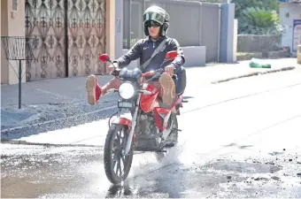  ??  ?? Un motociclis­ta levanta las piernas para evitar que se mojen sus calzados con el agua que inunda el asfalto. El bache con la pérdida de agua está en la Av. Rodríguez de Francia y Parapití.