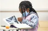  ??  ?? A secondgrad­er reads a book at the program, which provides masks and checks temperatur­es.