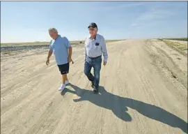  ?? Robyn Beck AFP/Getty Images ?? RAUL GOMEZ, left, and Greg Ojeda near Cross Creek levee in the Central Valley town of Corcoran. The levee was rebuilt in 2017 after sinking 7 feet since 1983.