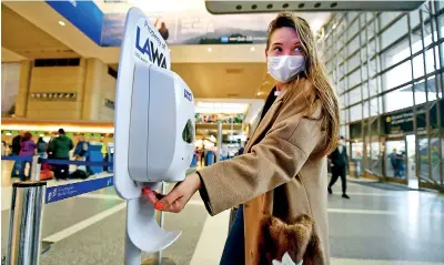  ??  ?? A woman wearing a facemask uses hand sanitizer on arrival at Los Angeles Internatio­nal Airport. (AFP)