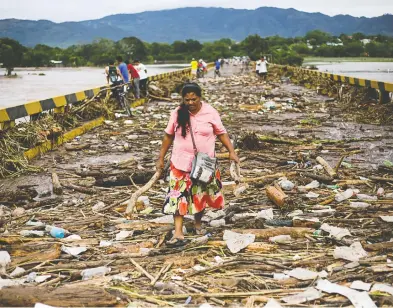  ?? JORGE CABRERA / REUTERS ?? A woman walks among debris on a bridge over the Chamelecon River after the passage of Storm Eta, in Pimienta,
Honduras Friday. Mudslides and flooding have killed and stranded hundreds.