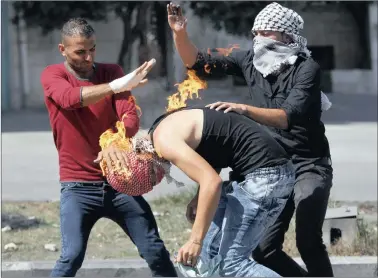  ?? PICTURE: MUSSA QAWASMA / REUTERS ?? ON FIRE: Palestinia­n protesters put out a fire burning on a compatriot caused by a petrol bomb that he was trying to throw at Israeli troops during clashes in the West Bank city of Hebron yesterday.