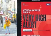 ??  ?? Pedestrian­s walk past an electronic billboard with a government message displaying the Covid-19 alert level in London.