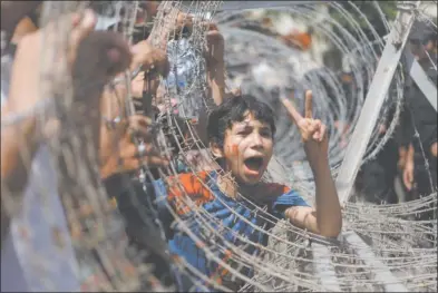  ?? AMR NABIL AP PHOTO ?? An Egyptian boy, his face painted with the number 25, the date of the Egyptian revolution, peers out of barbed wire during a protest in front of the Supreme Constituti­onal Court in Cairo Thursday. Egypt’s highest court dissolved the popularly elected...