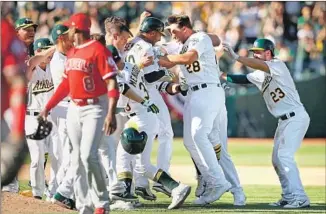  ?? Ezra Shaw Getty Images ?? JUBILANT ATHLETICS converge at home plate after Marcus Semien’s single off Noe Ramirez in the 11th scored Boog Powell with the winning run in Oakland’s opening day win over the Angels.