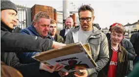  ?? Michael Steele / Getty Images ?? Wrexham owner Ryan Reynolds signs autographs and poses prior to the Emirates FA Cup fourth-round match between Wrexham and Sheffield United on Sunday.