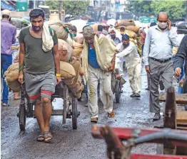  ?? — PTI ?? Labourers pull their carts with sacks on them during Unlock 2.0 at Chandni Chowk in New Delhi on Friday.
