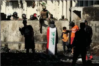  ?? The Associated Press ?? MOMENT OF CALM: Iraqi security forces and antigovern­ment protesters rest after both sides shake hands and converse in a rare moment of calm in hostilitie­s called to allow time for rest following clashes Saturday in Baghdad, Iraq.