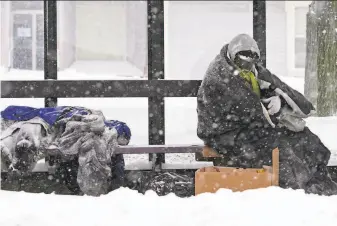  ?? Elise Amendola / Associated Press ?? A homeless man takes shelter at a bus stop in Lawrence, Mass. The Northeast’s first snowstorm broke records in cities and towns across the region as snow fell at more than 4 inches per hour.