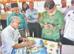  ??  ?? Riot puts his autograph on his 2017 calendar, as some staff members of SMK Serian look on.