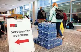  ?? GETTY IMAGES GAVIN JOHN/AFP VIA ?? A sign directing wildfire evacuees tp services available to them stands next to a pallet of bottled water Friday at the airport in Calgary, Alberta. The evaucation orders in Northwest Territorie­s and British Columbia marked the latest chapter of a terrible summer for wildfires in Canada, with tens of thousands of people forced to leave their homes and vast swathes of land scorched.