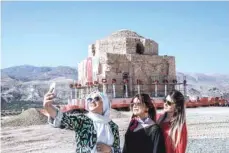  ?? — AFP ?? Women take a selfie picture as the Artuklu Hamam, a centuries-old bath house is loaded onto a wheeled platform and moved down a specially constructe­d road on Monday.