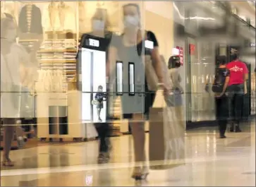  ?? Photog r aphs by Genaro Molina Los Angeles Times ?? A YOUNG GIRL peers inside as customers, seen through a ref lection, return to indoor shopping last week at the newly reopened Westfield Santa Anita mall in Arcadia. The mall’s stores are working at 25% capacity.