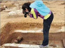  ??  ?? Yan Ni takes photos of unearthed relics at the excavation site in Hechuan.