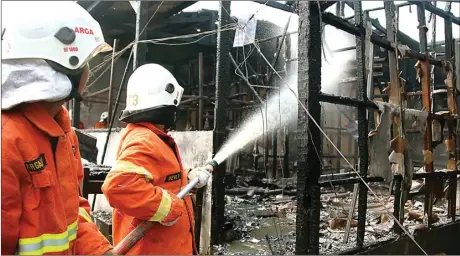  ?? MIRZA AHMAD/JAWA POS ?? TINGGAL RANGKA: Petugas pemadam kebakaran melakukan pembasahan pada bangunan semiperman­en di Jalan Kedungbaru­k yang terbakar kemarin (13/10).