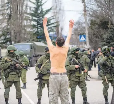  ?? ANDREW LUBIMOV/AP ?? Russian soldiers confront a bare-chested Ukrainian protester in 2014 in the Crimea during invasion by Russia's Vladimir Putin (below), an aggression that President Trump now seems to find OK.