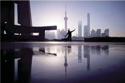  ??  ?? SHANGHAI: A man practice Tai Chi with a sword during sunrise at the promenade on the Bund along the Huangpu River, seen against the skyline of the Lujiazui Financial District in Pudong, Shanghai yesterday. —AFP