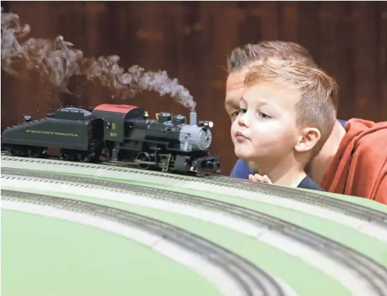  ?? PHOTOS BY BARBARA J. PERENIC/COLUMBUS DISPATCH ?? Rocco Jasinski, 2, and his father Dan, of Blacklick, watch an O-gauge steam locomotive chug by on a layout by the Buckeye Division Toy Train Operating Society.