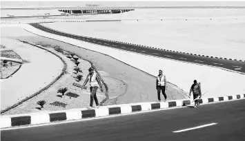  ??  ?? Constructi­on workers walk on the side of a newly-built road in Egypt’s new administra­tive capital.