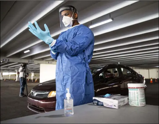  ?? Chase Stevens/Las Vegas Review-Journal @csstevensp­hoto ?? Nevada National Guard Spc. Demetrie Barnett puts on a fresh pair of gloves before taking a throat-swab sample last week during a preview of the drive-thru COVID-19 testing site at Texas Station. The site will operate Thursdays through Mondays.