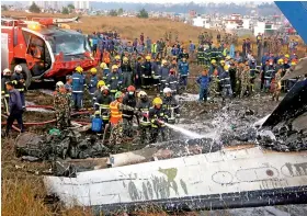  ??  ?? — PTI Nepalese firemen spray water on the debris after a passenger plane from Bangladesh crashed at the airport in Kathmandu, Nepal, on Monday.