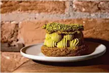  ?? ?? Customers commune with the pastry case at Maison Nico, top. A faithful companion, from far left, waits outside the cafe-bakery on Montgomery Street in S.F.; owners Andrea and Nicolas Delaroque at the shop; Paris-Brest includes pistachio cream and pistachio praline between two layers of choux covered with a pistachio crumble.