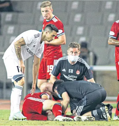  ??  ?? Andrew Considine is tended to by Aberdeen’s medical team after going down injured in Baku