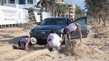  ?? JOE CAVARETTA/STAFF PHOTOGRAPH­ER ?? The Chance family tries to dig out after getting stuck on sandswept State Road A1A in Fort Lauderdale on Monday.