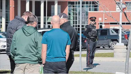  ?? JOHN RENNISON THE HAMILTON SPECTATOR ?? A police officer guards the entrance to the Bishop Ryan parking lot as staff wait nearby following a bomb call at the school Tuesday morning.