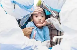  ?? CHINATOPIX ?? A child reacts to a throat swab Tuesday during mass testing for COVID-19 in Wuhan in China’s Hubei province. The country is fighting its most serious outbreak since last year.