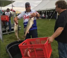  ?? RICHARD PAYERCHIN — THE MORNING JOURNAL ?? Buck Gehm of Crivitz, Wis., center, gets ready to set two of his team’s walleye in the carry basket after taking photos at the Cabela’s National Team Championsh­ip walleye tournament in Lorain on June 9.