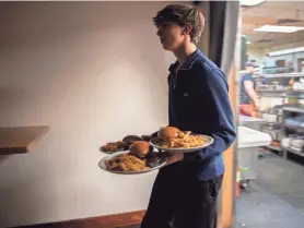  ?? ?? UNC Asheville student Dylan Machi, a food runner at Avenue M, carries three plates of food as he helps a server deliver orders to a table of eight at Avenue M in Asheville, on Feb. 7. Machi is included in the servers’ tip share.