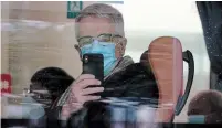  ?? NG HAN GUAN THE ASSOCIATED PRESS ?? A member from the World Health Organizati­on team of experts uses his smartphone to record the scene after boarding a bus to leave at the end of a two-week quarantine at a hotel in Wuhan in central China’s Hubei province on Thursday.