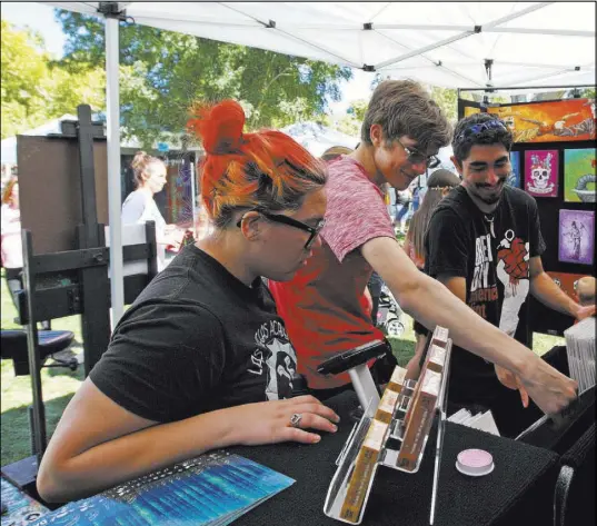  ??  ?? From left, Ana-Michele Johnson, 16, Alexander Metzger, 18 and Michael Donohue, 18, look at smaller prints of artist David Lozeau’s work during the Boulder City festival. Gabriella Benavidez Las Vegas Review-Journal @latina_ish