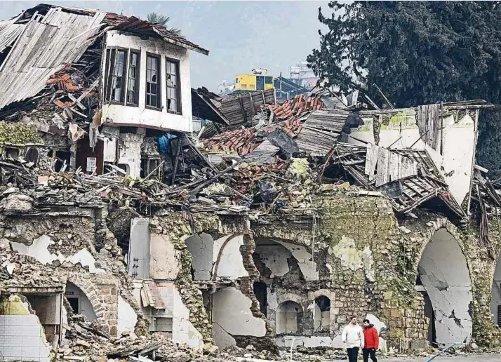  ?? Fotos: Boris Roessler/dpa ?? Zwei Männer gehen an einer völlig zerstörten Häuserzeil­e in Antakya vorbei.