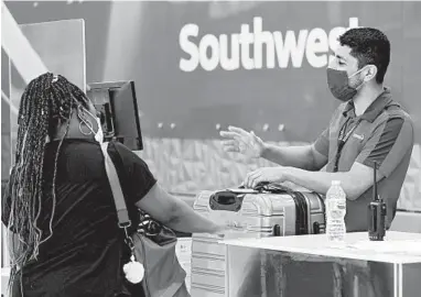  ?? TONY GUTIERREZ/AP ?? A Southwest Airlines employee helps a passenger at the ticket counter in June at Love Field in Dallas.