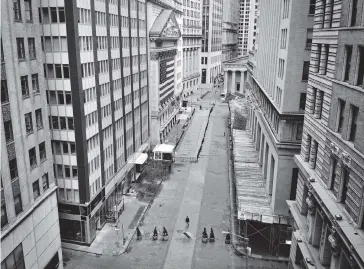  ?? JOHN MINCHILLO AP ?? A lone pedestrian wearing a protective mask walks past the New York Stock Exchange as COVID-19 concerns empty a typically bustling downtown area Saturday in New York.