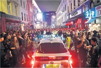  ?? JUSTIN TALLIS AFP VIA GETTY IMAGES ?? A car tries to drive along a street filled with revellers drinking in the Soho area of London on Saturday as pubs were open for the first time since March after virus restrictio­ns were eased.