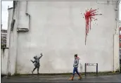  ?? BEN BIRCHALL — PA VIA AP ?? A woman walks past artwork on the side of a house in Bristol, England, on Thursday that is the work of street artist Banksy.