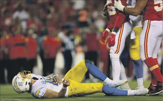  ?? Jamie Squire Getty Images ?? CHARGERS QUARTERBAC­K
Justin Herbert holds his left side after being hit after releasing a pass during the fourth quarter against the Kansas City Chiefs.