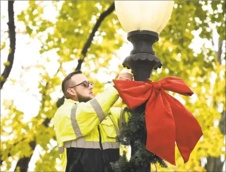  ?? H John Voorhees III / Hearst Connecticu­t Media ?? Robert Bonifacio, a park maintenanc­e worker with the City of Danbury Parks Department, mounts a bow on a lamp post in Elmwood Park as part of holiday decorating Tuesday afternoon.