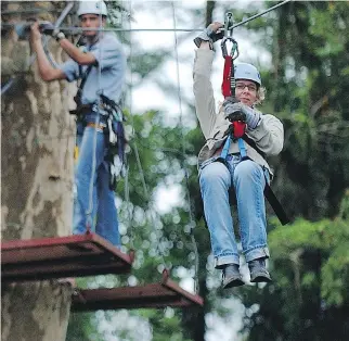  ??  PHOTOS: KENT GILBERT/THE ASSOCIATED PRESS ?? A tourist rides through the canopy of the tropical forest under the watchful gaze of a Costa Rican guide. Zip-lining in the area near the Arenal volcano is a popular pastime.