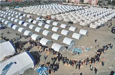  ?? HUSSEIN MALLA/AP FILE ?? People who lost their houses in the Feb. 6 earthquake line up to receive aid supplies at a makeshift camp in the Turkish city of Iskenderun last month.