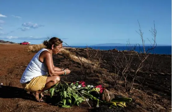  ?? BRYAN ANSELM/THE NEW YORK TIMES ?? A woman placed flowers on a hillside overlookin­g Lahaina, Hawaii, which was mostly destroyed by the wildfire.