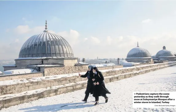  ?? Chris McGrath/Getty Images ?? Pedestrian­s capture the scene yesterday as they walk through snow at Suleymaniy­e Mosque after a winter storm in Istanbul, Turkey