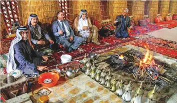  ?? AFP ?? Members of an Iraqi clan gather inside a straw tent (top) while another enters the tent (left) in the town of Mishkhab, south of Najaf. For centuries, Iraqi clans have used their own system to resolve disputes, with tribal dignitarie­s bringing together opposing sides to mediate in de facto ‘hearings’. If one side failed to attend, the rival clan would fire on the absentee’s home or his fellow tribesmen’s as a ‘tribal warning’.