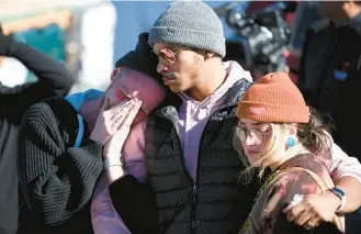  ?? JASON CONNOLLY/GETTY-AFP ?? Tyler Johnston, left, Keenan Mastes-Holmes and Altas Pretzeus pay their respects on Sunday at a makeshift memorial in Colorado Springs, Colo., for victims of a mass shooting at a gay nightclub late Saturday night.