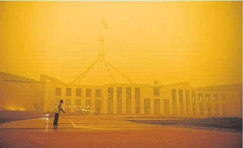  ?? REUTERS ?? A man cleans the forecourt of Parliament House surrounded by smoke in Canberra, Australia.