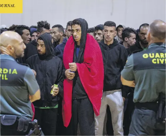  ?? EMILIO MORENATTI / THE ASSOCIATED PRESS ?? Spanish officers stand guard as migrants gather at a makeshift emergency centre in Barbate, in the south of Spain, after being rescued by the country’s Maritime Rescue Service in the Strait of Gibraltar on Thursday.